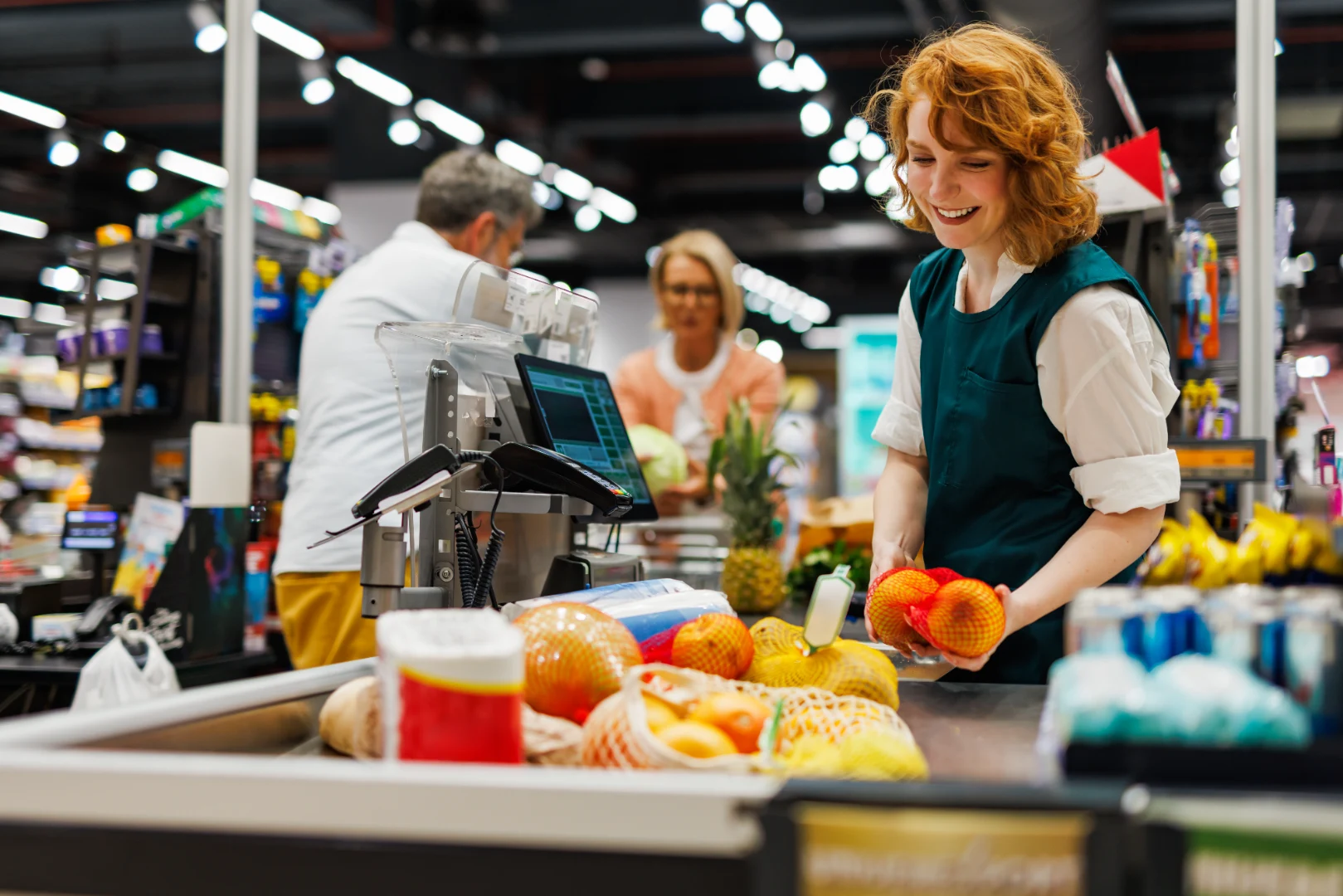 A smiling cashier scanning fresh fruit at a supermarket checkout